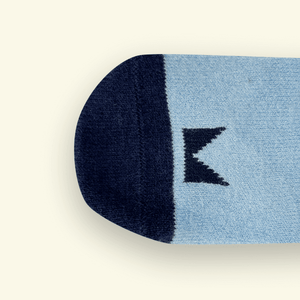 Close-up of Mosey by Lamington merino baby socks in blue and navy showing knit texture and logo detail.