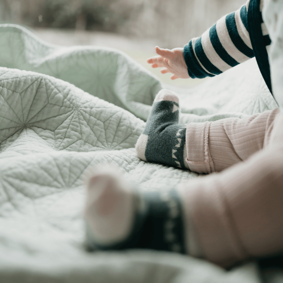 Baby wearing Mosey by Lamington merino baby socks in forest green with geometric pattern.