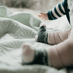 Baby wearing Mosey by Lamington merino baby socks in forest green with geometric pattern.