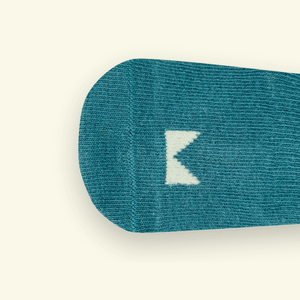 Close-up of Mosey by Lamington teal organic cotton baby socks in teal showing rib knit texture and logo detail.