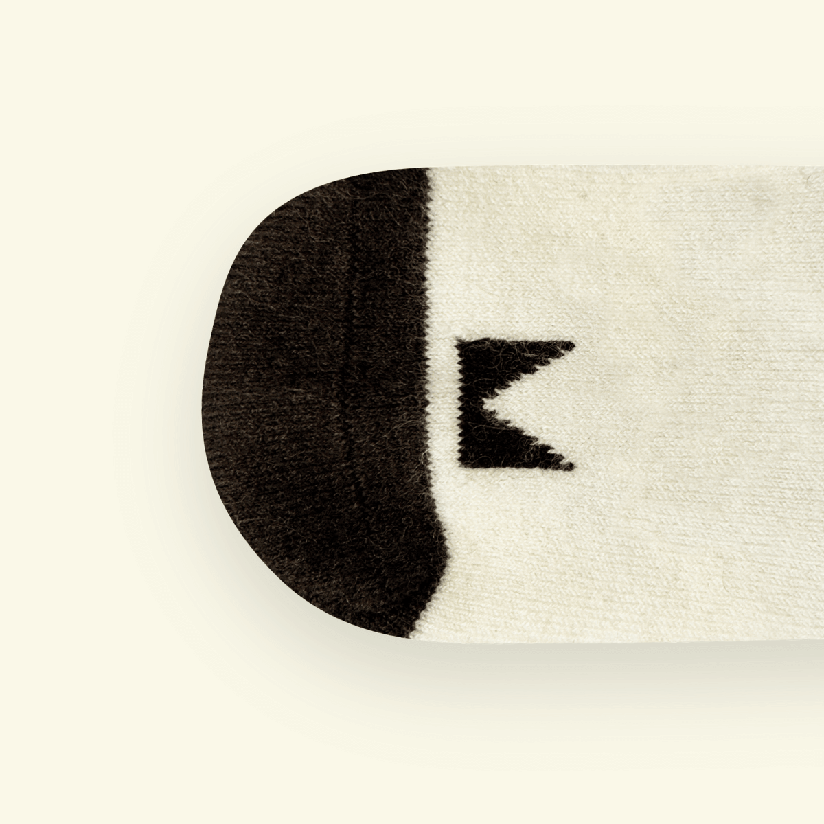 Close-up of Mosey by Lamington merino baby socks in cream with black pattern showing logo detail.