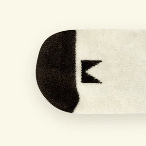 Close-up of Mosey by Lamington merino baby socks in cream with black pattern showing logo detail.