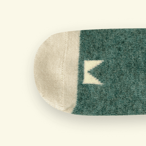 Close-up of Mosey by Lamington merino baby socks in forest green showing knit texture and logo detail.